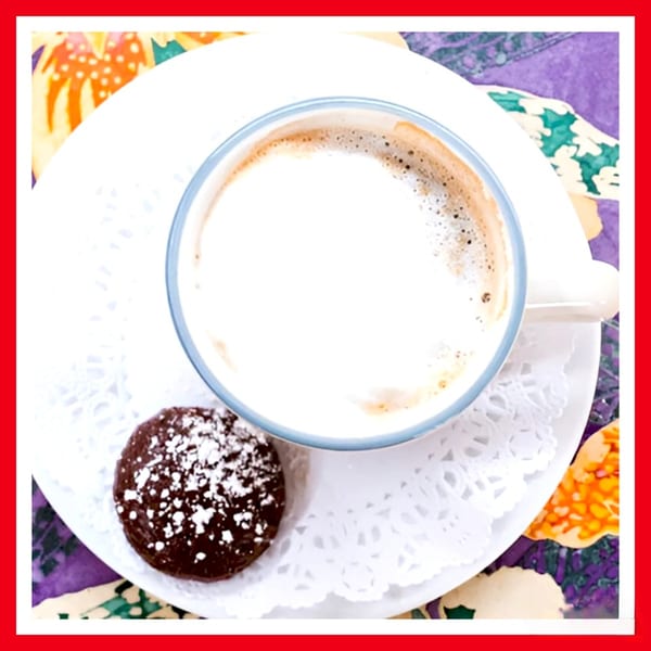 Overhead view of a Crazy Burger cappuccino with a chocolate cookie dusted with powdered sugar.