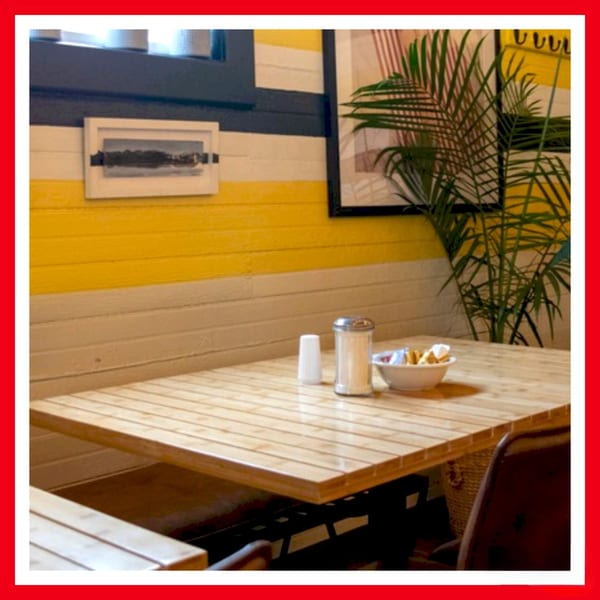 A wooden table with condiments and a bowl of crackers sits in a Crazy Burger restaurant booth.