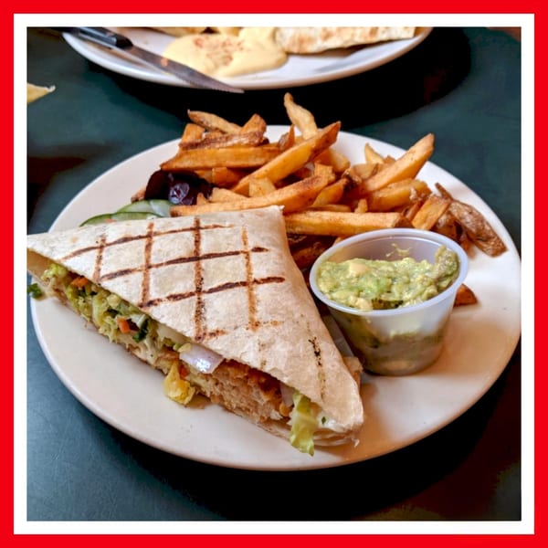 A grilled wrap filled with vegetables and chicken, served with fries and guacamole on a white plate.