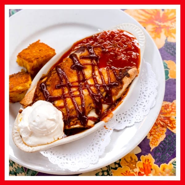 Crazy Burger's enchiladas with red sauce, BBQ drizzle, sour cream, and cornbread on a floral placemat.