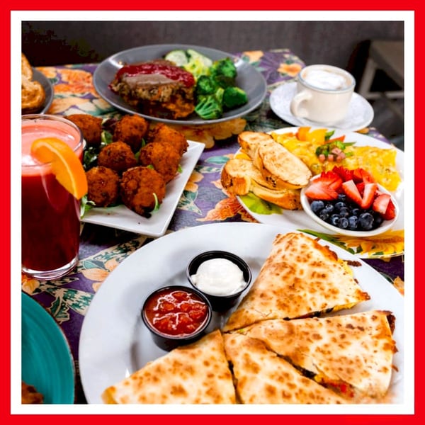 A table laden with various dishes including quesadillas, meatballs, meatloaf, and a fruit cup.