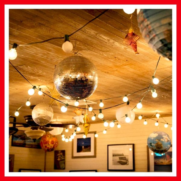 A disco ball and string lights hang from a wooden ceiling inside Crazy Burger restaurant.